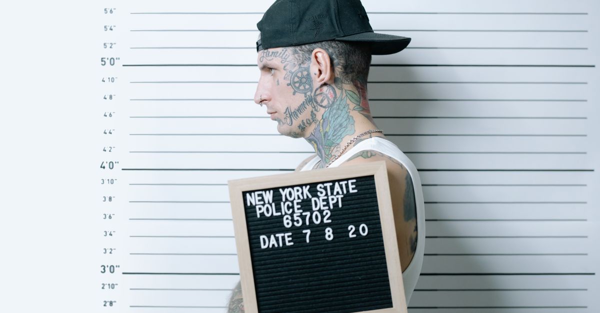 Side view of tattooed man holding mugshot board in police lineup.
